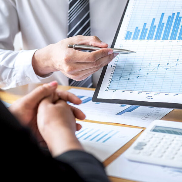 Business meeting showing financial graphs on paper and a tablet, with hands in discussion.