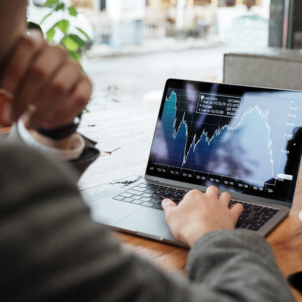 Person analyzing stock market data on a laptop screen in a cafe or office setting.