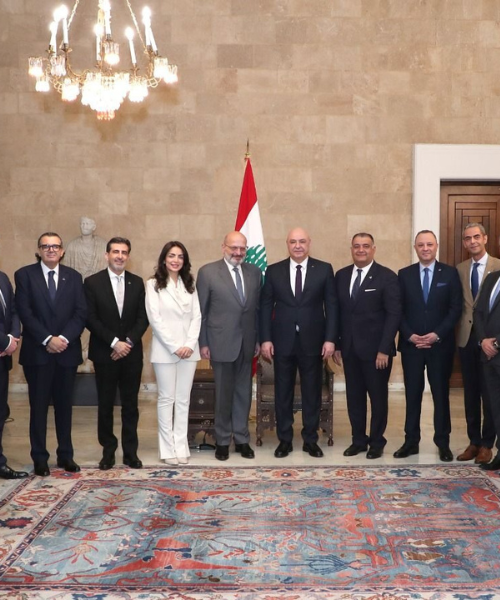 Delegates pose for a formal group photo with Lebanese flag in official meeting room.